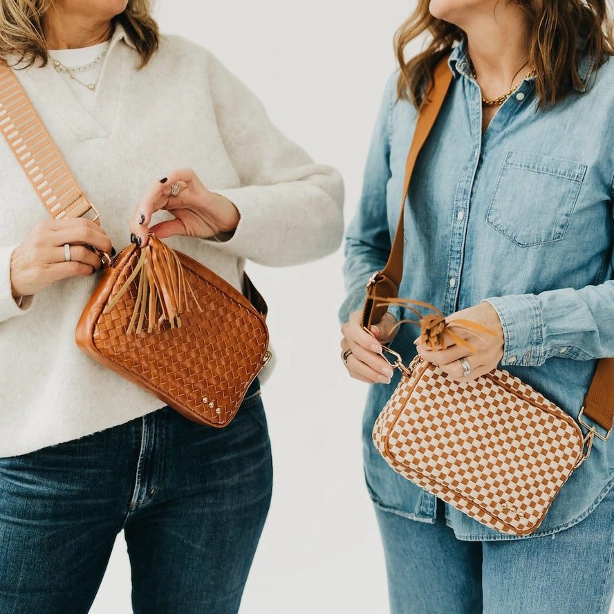 Two women holding brown woven handbags against a plain background