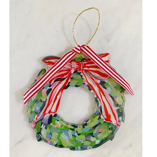 A hand-painted glass Christmas wreath ornament with a red and white striped ribbon bow and gold hanging loop, set against a light marble background.