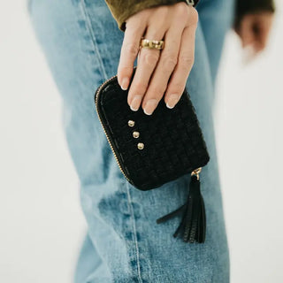 Black quilted wallet with gold buttons held by a person wearing blue jeans.