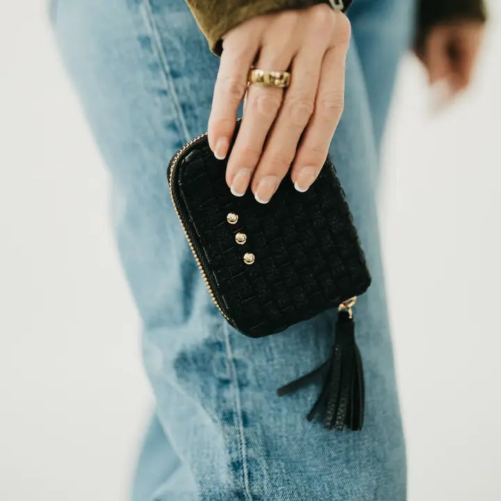 Black quilted wallet with gold buttons held by a person wearing blue jeans.
