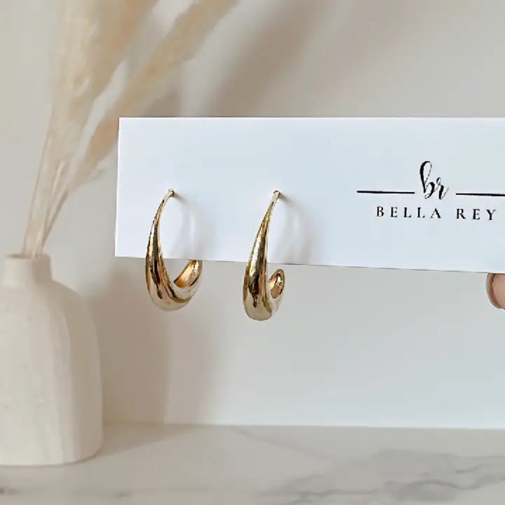 Gold hoop earrings on a Bella Rey branded card with a vase in the background