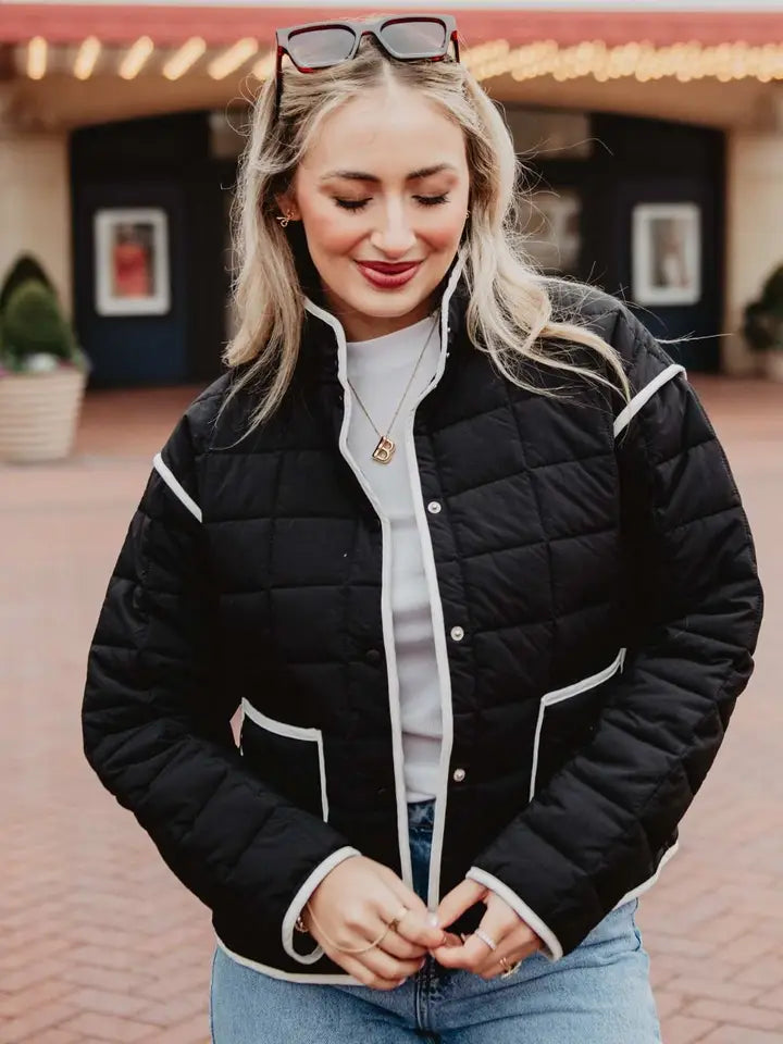 Woman wearing a black quilted jacket with white trim outdoors.