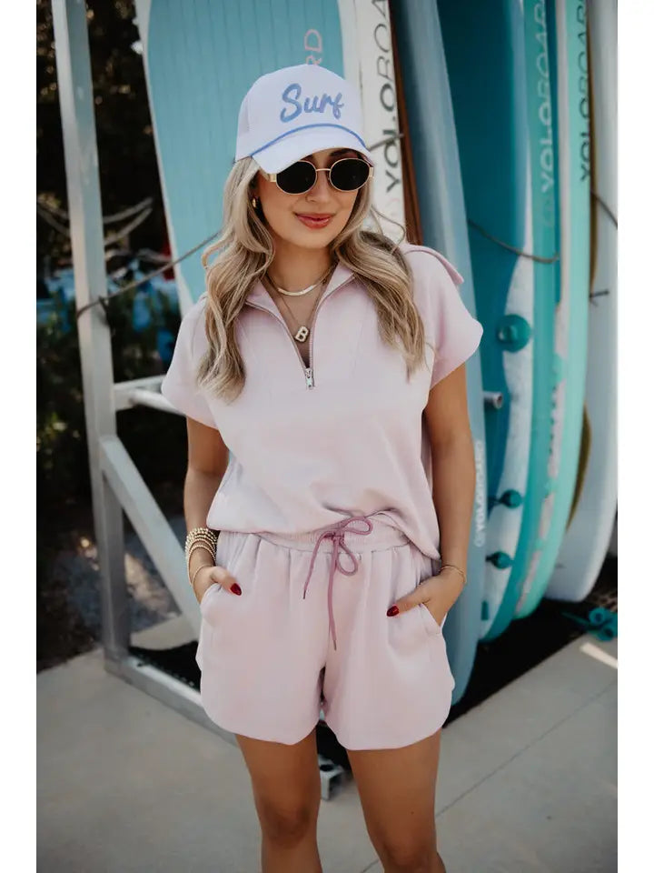 Woman in pink outfit with 'Surf' cap standing in front of surfboards