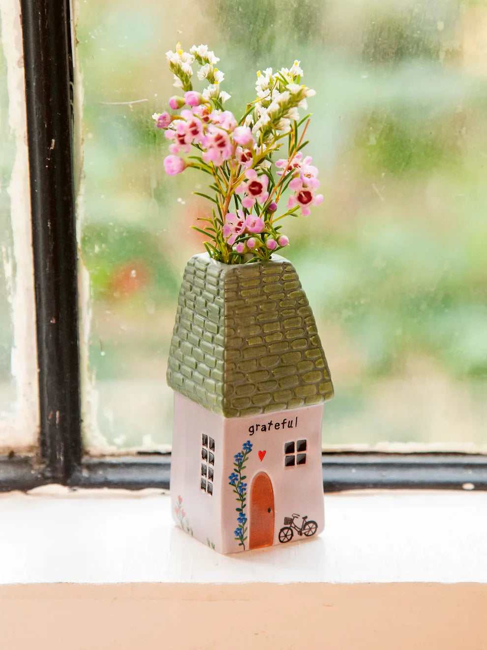 Decorative vase shaped like a house with flowers on a windowsill