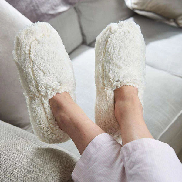 White fluffy slippers worn by a person sitting on a couch.