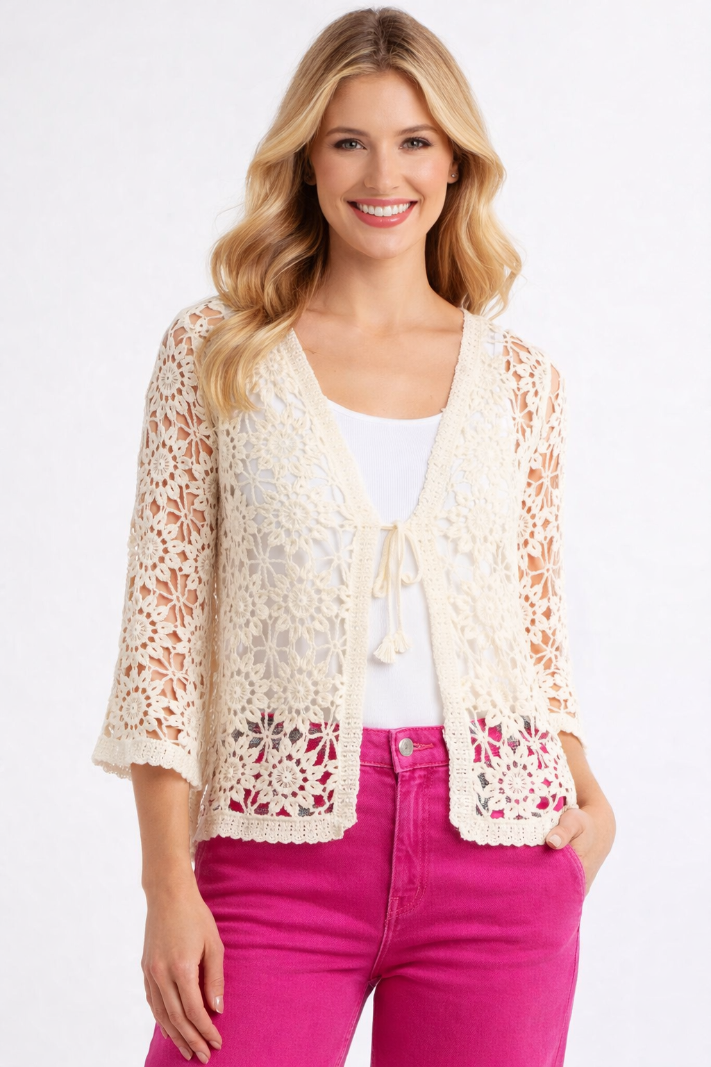 Woman wearing a white lace cardigan over a white top and pink pants on a white background