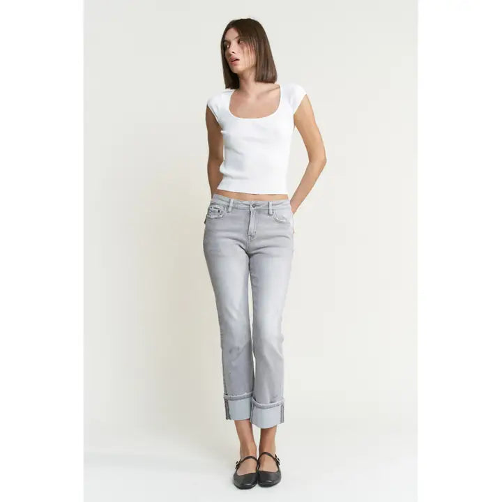 Woman wearing a white tank top and light blue jeans on a plain background