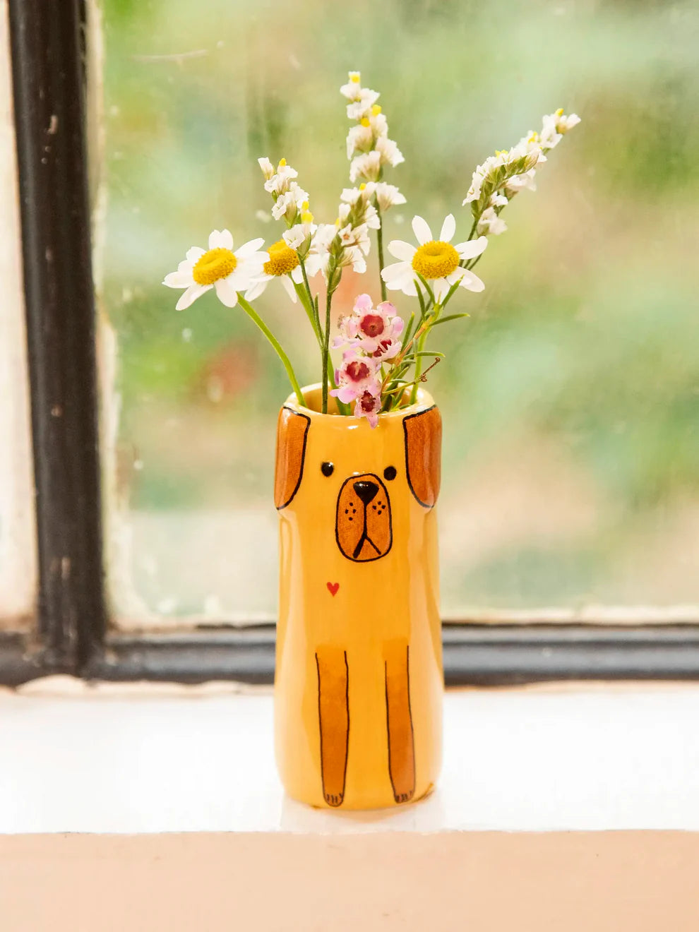 Dog-shaped vase with flowers in front of a window