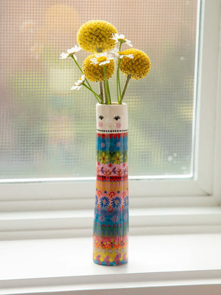 Colorful vase with a face design holding flowers on a windowsill.