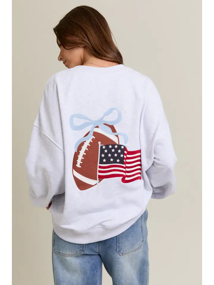 Person wearing a light gray sweatshirt with a football and American flag design on the back.