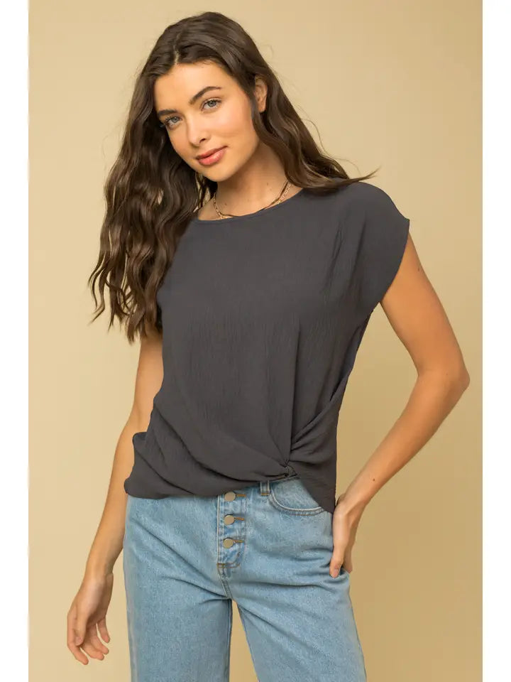 Woman wearing a dark gray top and light blue jeans against a beige background