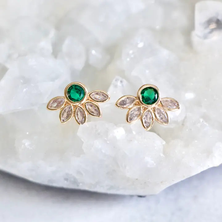 Gold earrings with green gemstones on a white shell background