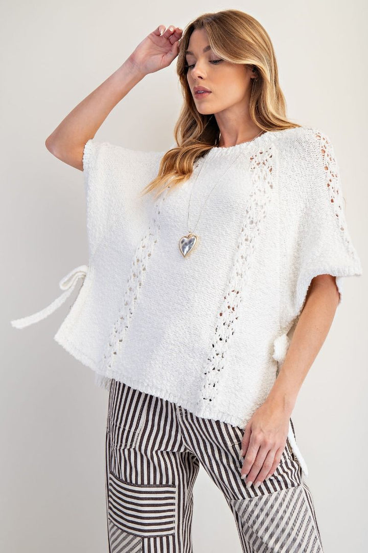 Woman wearing a white knitted poncho with black patterns against a plain background