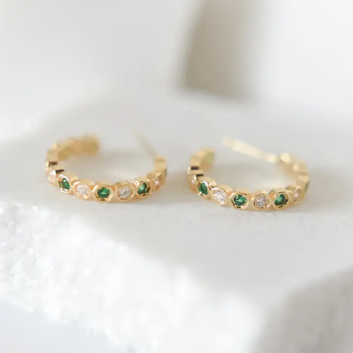 Gold hoop earrings with green gemstones on a white background