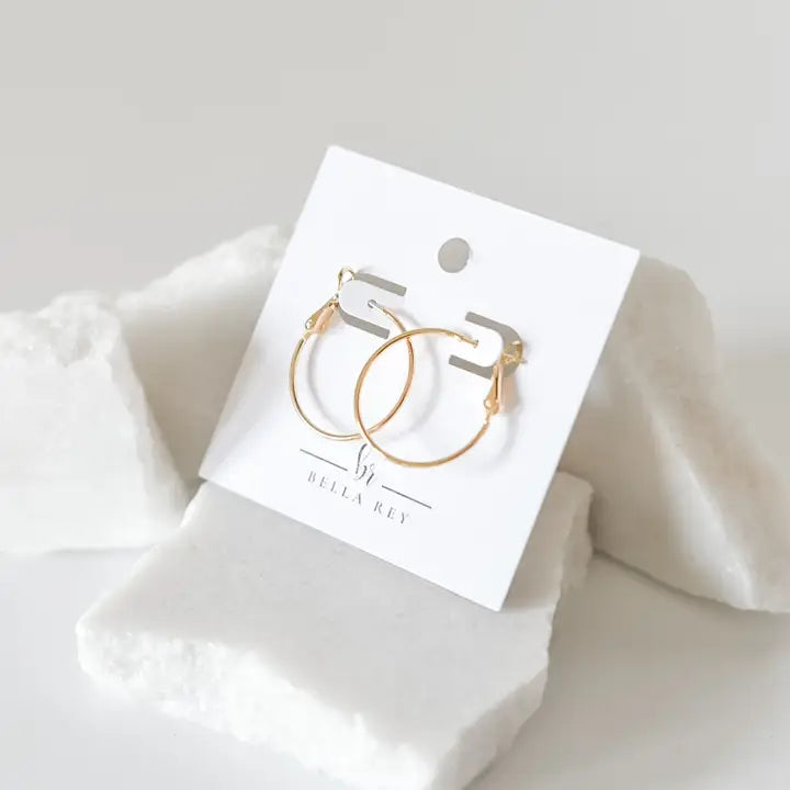 Gold hoop earrings on a branded card with a soft white background