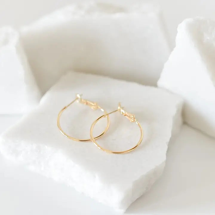 Gold hoop earrings on a soft white fabric background