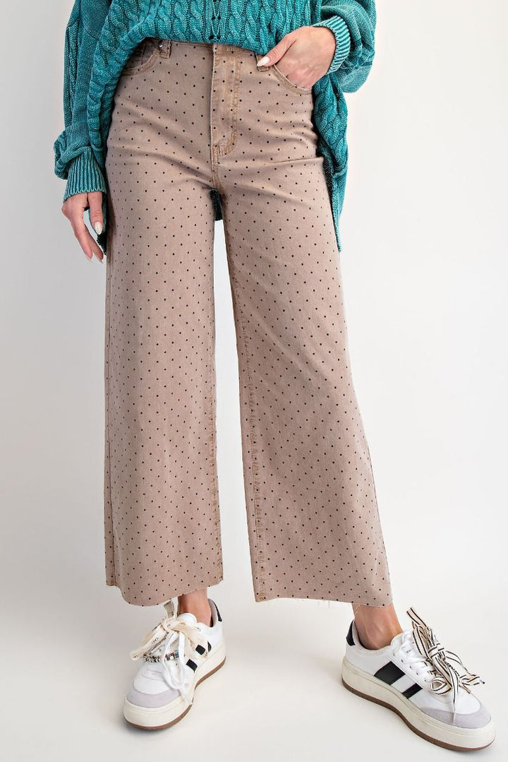 Person wearing beige polka dot pants with a teal sweater and white sneakers on a light gray background