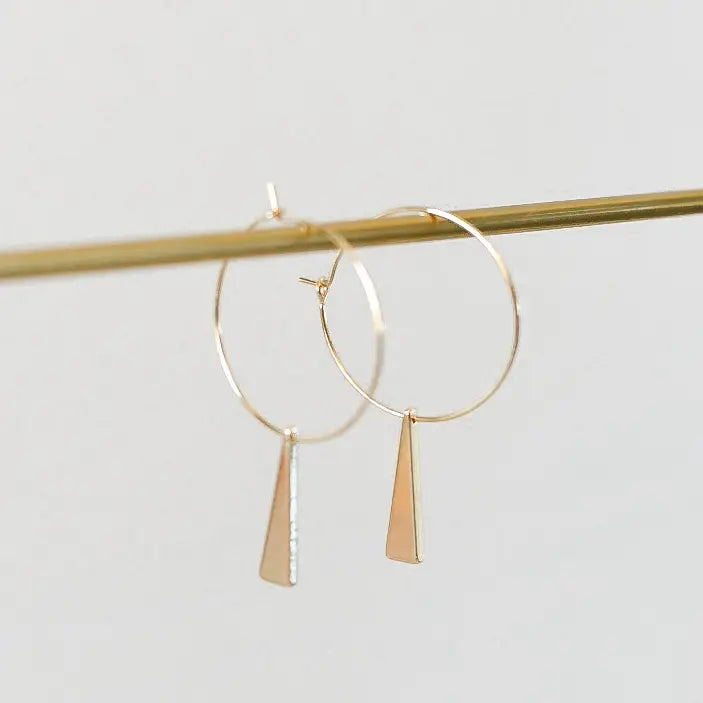 Gold hoop earrings with dangling triangles on a light gray background