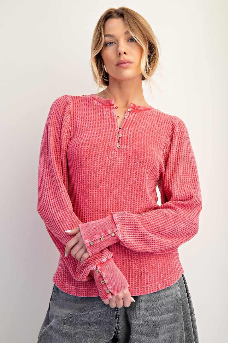 Woman wearing a pink textured sweater with button details on a plain background