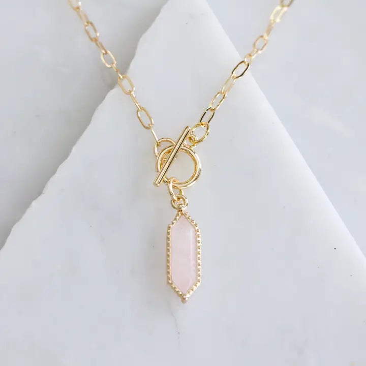 Gold necklace with a pink pendant on a white surface