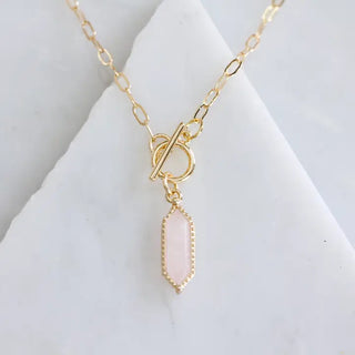 Gold necklace with a pink pendant on a white surface