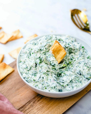 A bowl of spinach artichoke dip with a crouton on top, served with crackers on the side.
