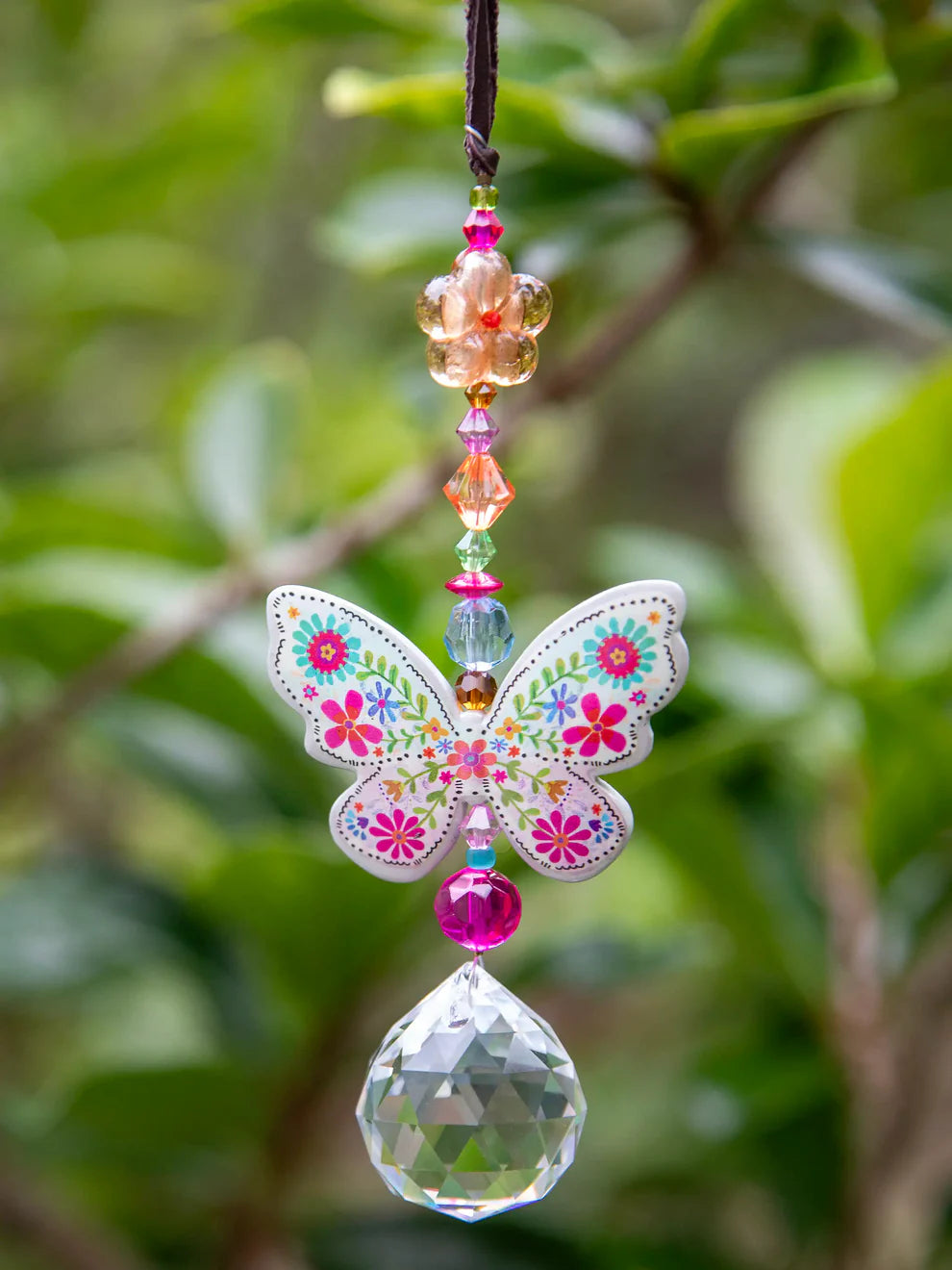 Decorative butterfly ornament with beads and crystal on a blurred green leaf background