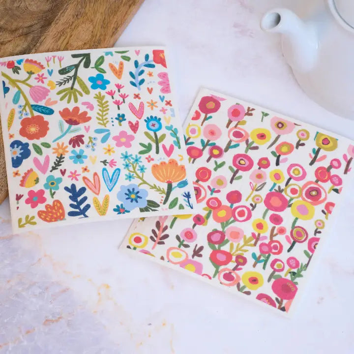 Two floral-patterned coasters on a white surface with a wooden block and teapot in the background.