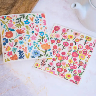 Two floral-patterned coasters on a white surface with a wooden block and teapot in the background.
