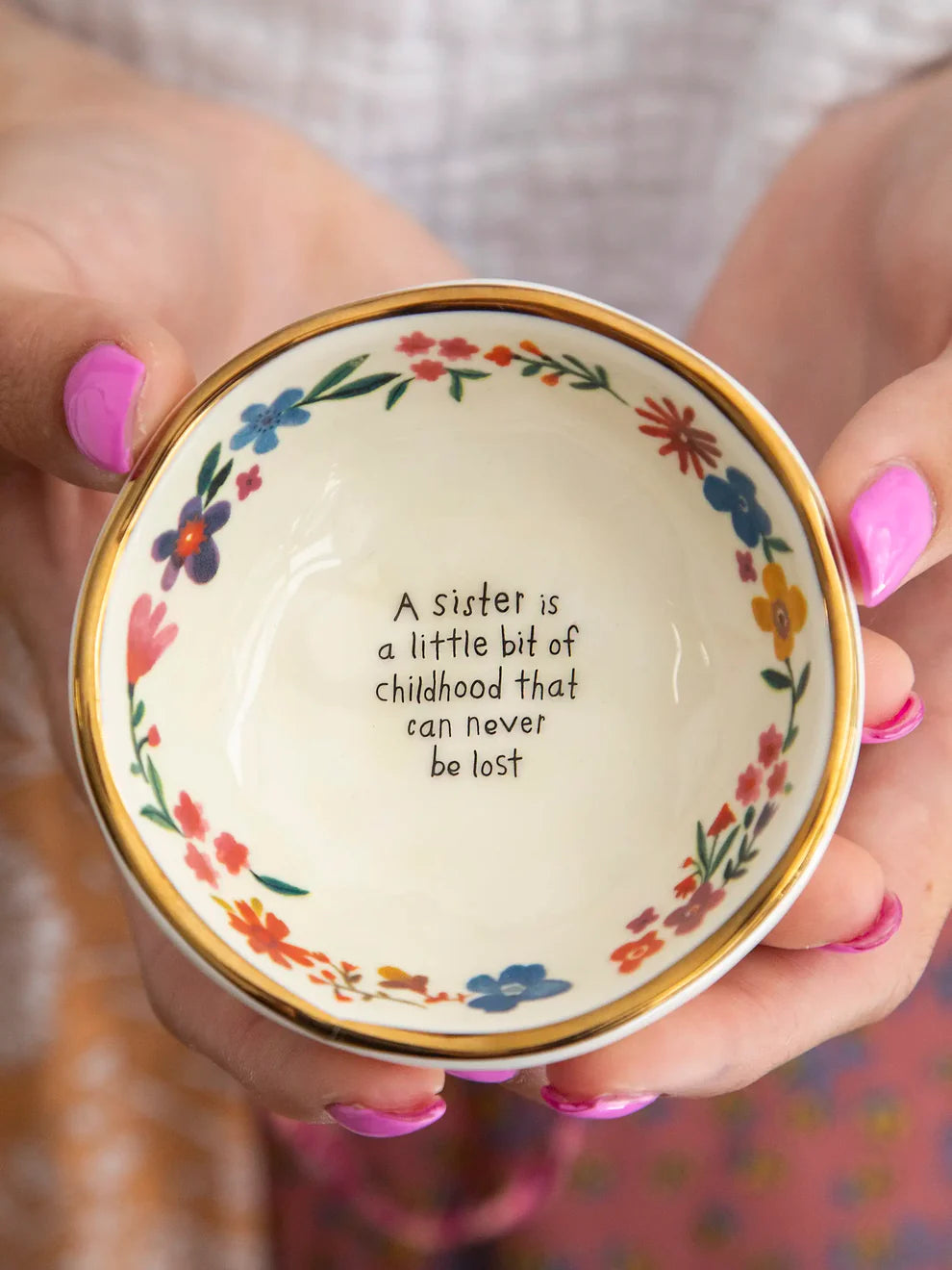 Decorative bowl held by hands with floral design and text