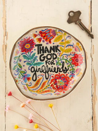 Decorative plate with floral design and 'Thank God for girlfriends' text on a wooden surface.