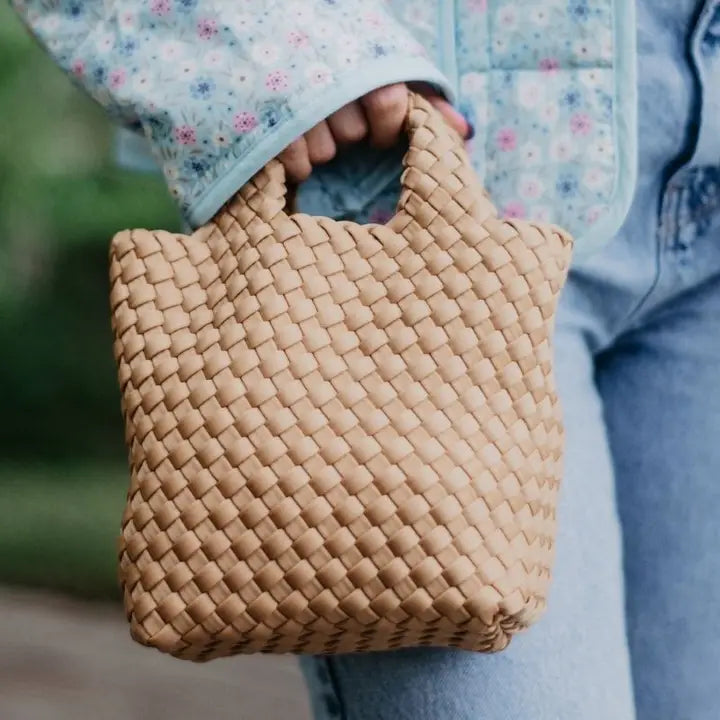 Person holding a woven beige handbag with a blurred background