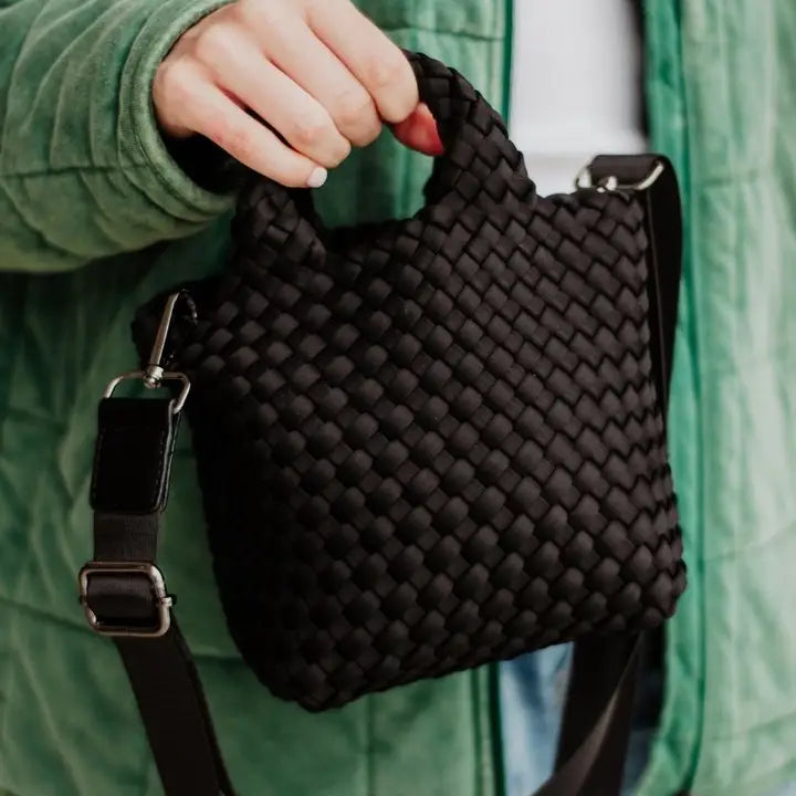 Black woven handbag held by a person wearing a green jacket.